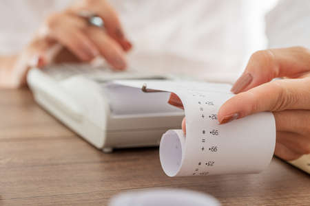 Closeup view of a bookkeeper holding receipt coming from an adding machine in a conceptual image of tax and finance.の写真素材