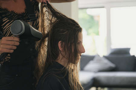 Hairdresser blow drying long hair of a young woman.の写真素材