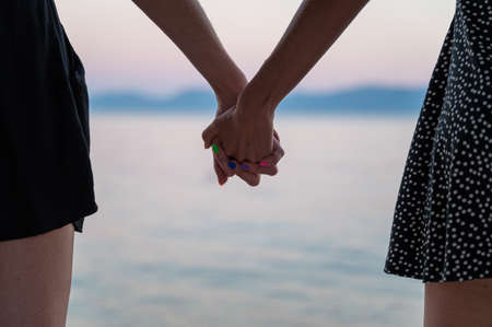 Closeup view of lesbian gay couple holding hands standing by the evening sea.の写真素材