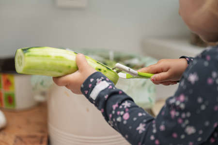 Closeup view of little toddler girl peeling cucumber with a peeler.の写真素材