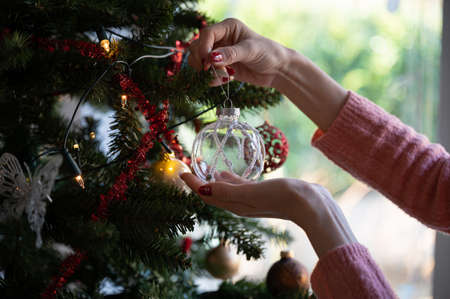 Closeup view of a woman with seasonal manicure hanging shiny transparent holiday bauble on christmas tree.の写真素材