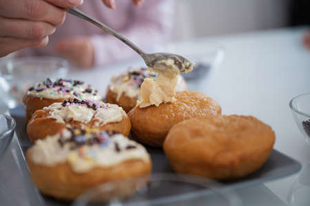Closeup view of a woman decorating delicious home made vegan doughnuts with white chocolate topping.の写真素材