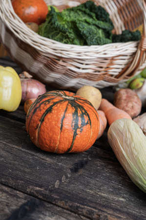 Variety of colorful autumn vegetables scattered from a wicker basket on rustic wooden boards.