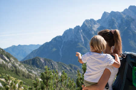 Young mother holding her toddler daughter  looking at beautiful view of mountains as they hike together on a sunny day.の写真素材