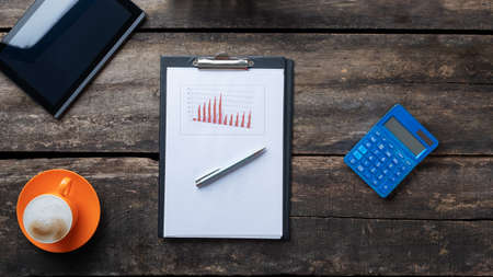 Top view of pen lying on a paperwork with graphs and charts on a desk next to digital tablet,...