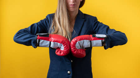 Front view of a businesswoman wearing red boxing gloves bumping fists together in a conceptual image of powerful women in business world. Over yellow background.の写真素材