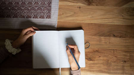 Top view of a woman writing and making notes in her blank stripped notepad on a wooden desk.の写真素材