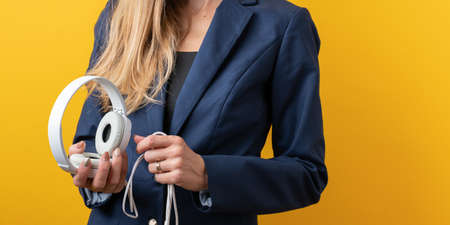 Closeup view of a woman in a suit holding headset in her hands. Over yellow background.