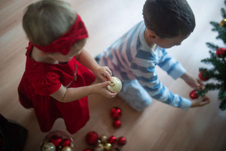 Top view of toddler children decorating holiday tree with red and gold christmas baubles.の写真素材