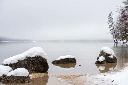 Calm winter nature - tranquil lake Bohinj with snow covered rocks looking out the water.の写真素材