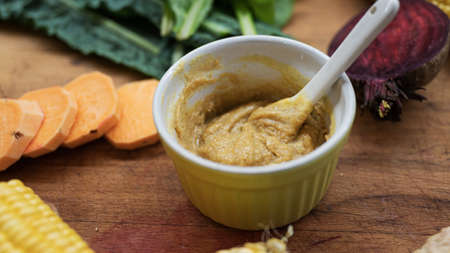 Cup of delicious healthy vegan gravy or dip placed on wooden cutting board full of colorful...