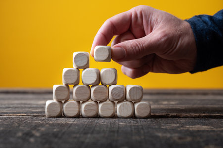 Male hand building a pyramid of wooden dices in a conceptual image.