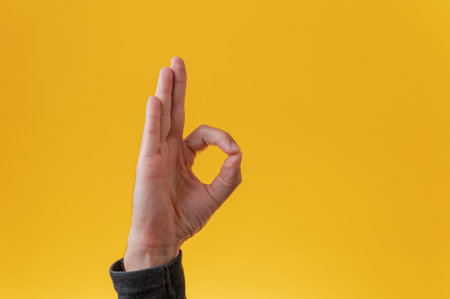 Male hand making on OK gesture over yellow background.の写真素材