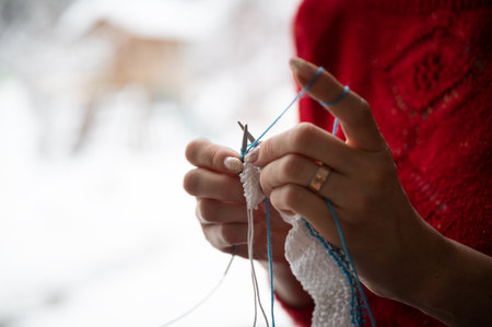 Closeup view of a woman knitting by the window withy snowy landscape outside.の写真素材