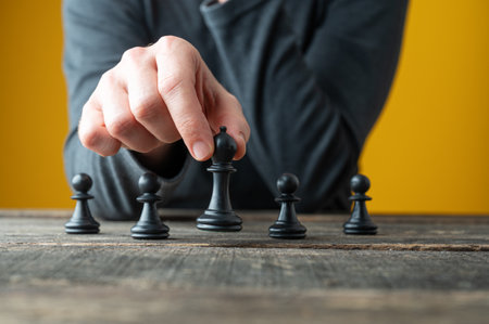 Conceptual image of strategy and power with male hand positioning chess pieces on rustic wooden board.の写真素材