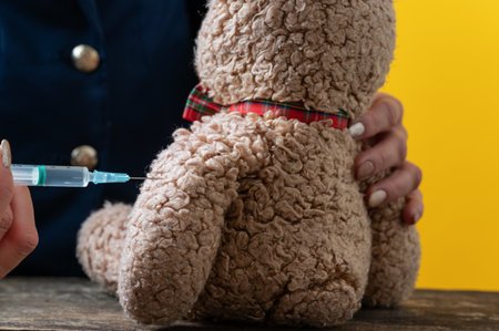 Closeup view of vaccinating teddy bear toy with medical syringe.