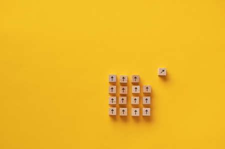 Wooden block with arrow on it separating from a group of other blocks in a conceptual image of vision and determination.の写真素材