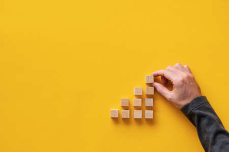 Male hand building stairway like structure with wooden blocks in a conceptual image. Over yellow background with copy space.の写真素材