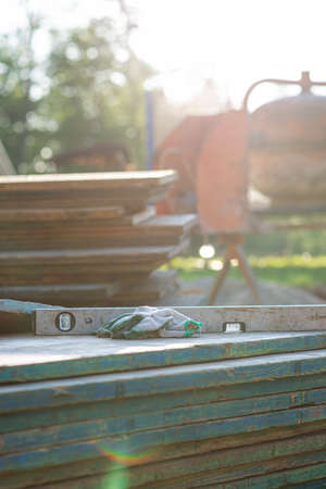 Working gloves and construction level placed on wooden panels with cement mixer in background lit by the sun.の写真素材