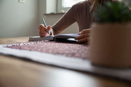 Low angle view of a woman, student, writing with pencil in notepad sitting at dinning table.の写真素材