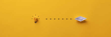 Wide view image of paper made origami boat sailing towards a light bulb in a conceptual image.の写真素材