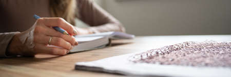 Wide view image of a woman writing in notebook on a home dining table.の写真素材