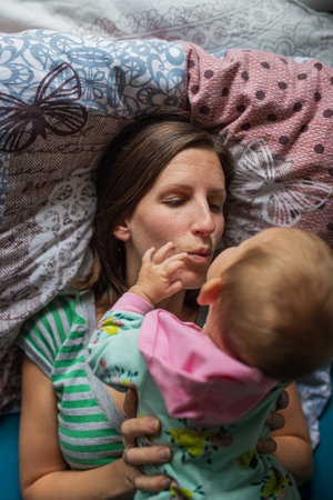 Young mother lying on the bed with her baby daughter lying on top of her in a tender moment between mother and daughter.の写真素材