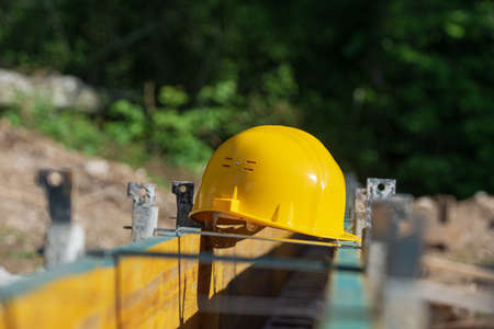 Yellow hardhat resting on a framework of wooden panels outside in a construction site.の写真素材