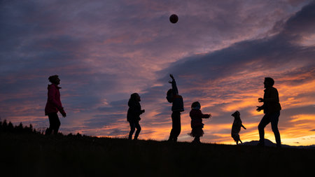 Silhouette of a family playing and having fun outside under beautiful cloudy sky at sunset.の写真素材