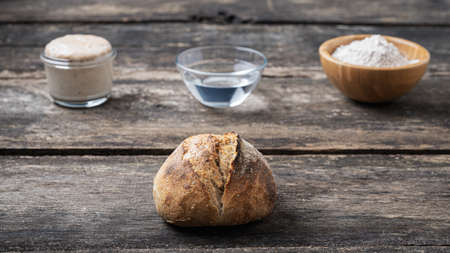 Still life with homemade sourdough bread bun and ingredients - starter yeast, water and flour.の写真素材