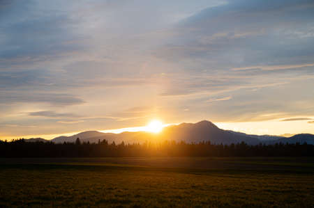 Beautiful sunset with the sun setting behind the distant hills with cloudy sky above.の写真素材