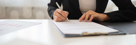 Wide view closeup image of a businesswoman signing a document or application form in a folder.