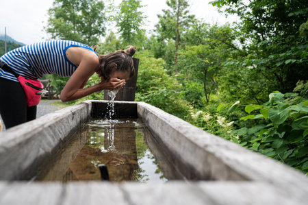 Young woman washing her face in a wooden trough placed in green nature.