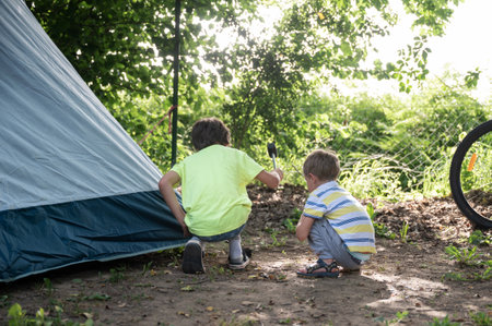 Two toddler boys hammering a spike for camping tent in the ground.の写真素材
