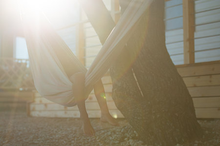 Childs legs looking out of a hammock hanging in summer tourist resort, lit by a bright morning sunflare.の写真素材