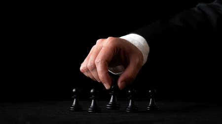 Hand of a businessman arranging chess figures in a conceptual image of leadership and power. Over black background.の写真素材