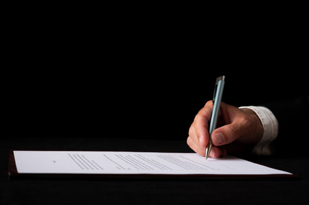 closeup view of a hand of a businessman signing a document or contract. Over black background.の写真素材