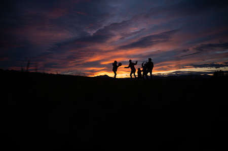 Silhouette of a family playing with a ball outside on a hill at sunset under beautiful cloudy sky...