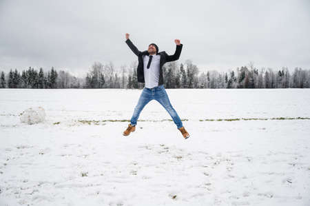 Young man in a business jacket jumping joyfully in the air outside in a beautiful snowy nature.