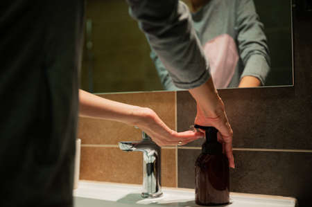 Low angle view of a woman squeezing soap on her hands from a soap dispenser to wash her hands in the bathroom.の写真素材