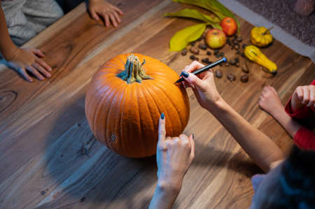 Top view of a mother and her kids drawing on a halloween pumpkin to mark where to cut it.の写真素材