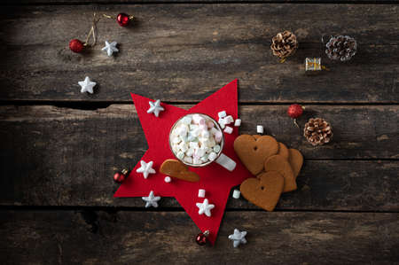 Top view of cup of hot chocolate heaping with sweet marshmallows placed on a red holiday star with cookies and christmas decoration around it.の写真素材