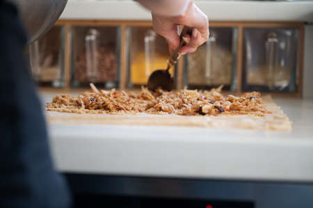 Low angle view of a woman making an apple strudel arranging the filling on the dough on kitchen counter.の写真素材