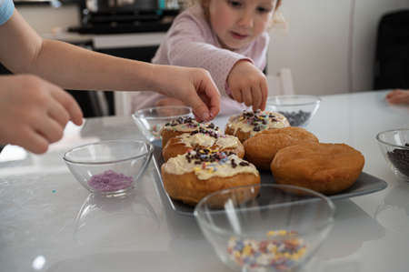 Toddler children decorating homemade vegan doughnuts with sprinkles and chocolate.