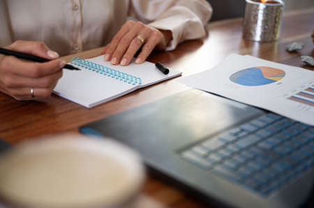 Low angle view of businesswoman writing in notepad with documents and report on her desk.