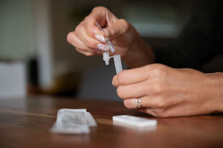 Closeup view of female hands holding testing solution tube of covid19 home self test kit in a conceptual image of coronavirus pandemic.の写真素材