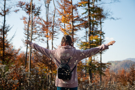 View from behind of a young woman standing in beautiful colorful autumn nature enjoying life with...