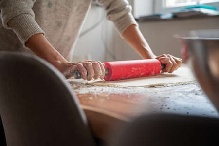 Low angle view of a woman rolling a homemade pastry dough with a rolling pin on a table.の写真素材