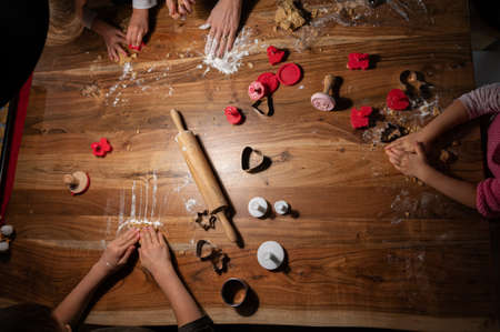 Top view of a family making christmas holiday shaped vegan cookies on a wooden table.
