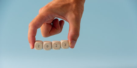 Male hand holding four wooden dices spelling 2023 over light blue background.の写真素材